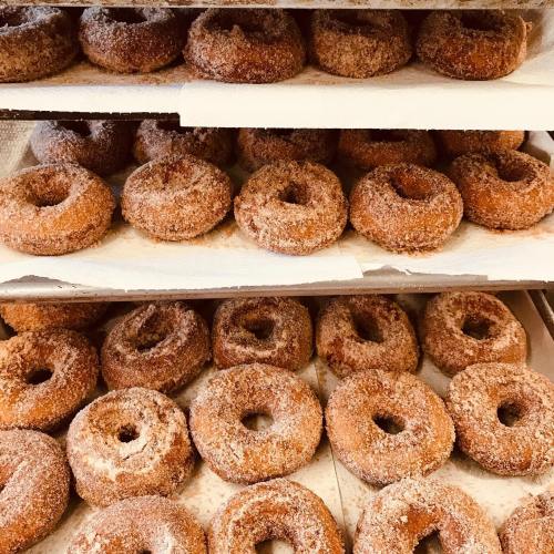A display of freshly made, cinnamon-sugar coated donuts stacked on trays.