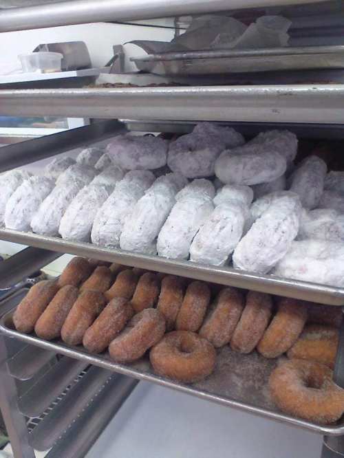 A metal rack filled with various types of donuts, some powdered and others glazed, arranged in neat rows.