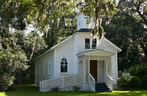 A charming white church with a steeple, surrounded by lush greenery and hanging moss.