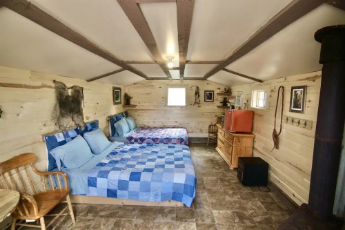 Cozy interior of a cabin featuring two beds, wooden furniture, and rustic decor on the walls.