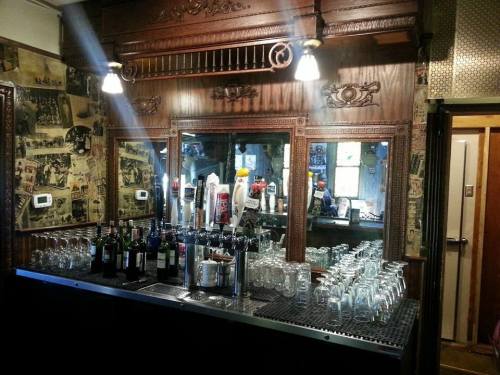 A vintage bar with wooden decor, glassware, and a mirrored back wall, illuminated by hanging lights.