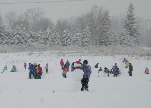 Children playing in a snowy field, building snowmen and enjoying the winter weather amidst falling snow.