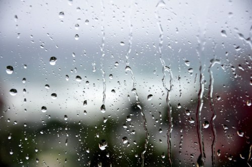 Raindrops on a window, blurring the view of a landscape beyond.