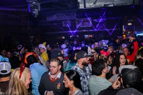A lively crowd at a bar, with people dancing and enjoying a festive atmosphere, colorful lights in the background.