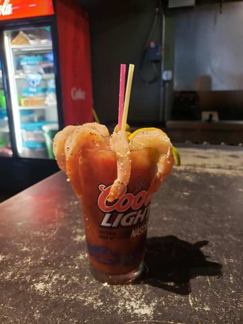 A cocktail glass filled with a drink, garnished with shrimp and lime, set on a dark countertop.