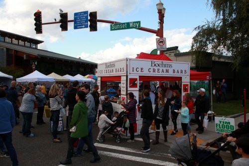 A busy street fair scene with a red ice cream bar stand and crowds of people enjoying the event.