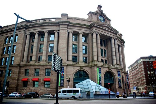 Historic building with a clock tower, featuring a glass pyramid entrance and urban surroundings.