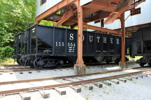 Two vintage black train cars labeled "SOUTHERN" parked under a structure, surrounded by greenery and gravel.
