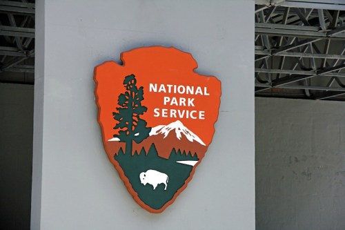 Logo of the National Park Service featuring a tree, mountain, and bison on an orange and green background.