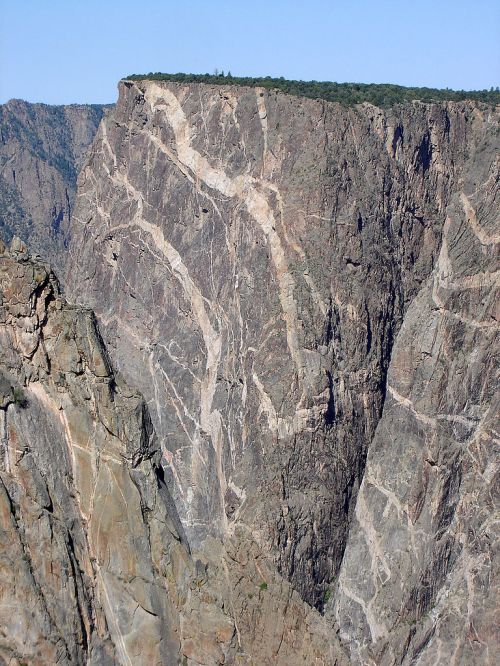 A steep, rocky cliff with visible geological layers and a clear blue sky above.