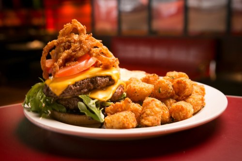 A juicy cheeseburger topped with crispy onions and tomatoes, served with a side of golden tater tots.