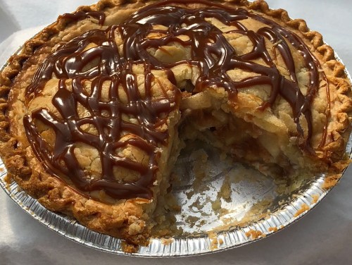 A freshly baked apple pie with a golden crust, drizzled with caramel, and a slice cut out.