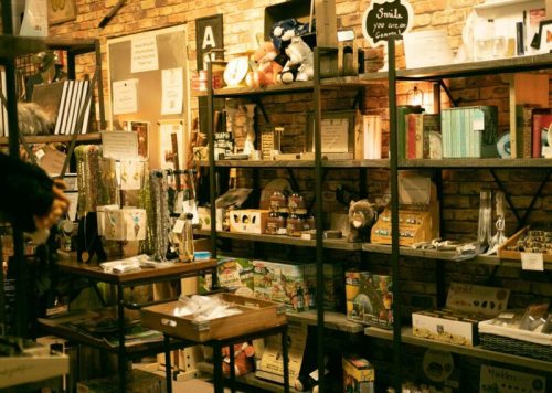 A cozy shop display with shelves filled with various decorative items, books, and gifts against a brick wall.