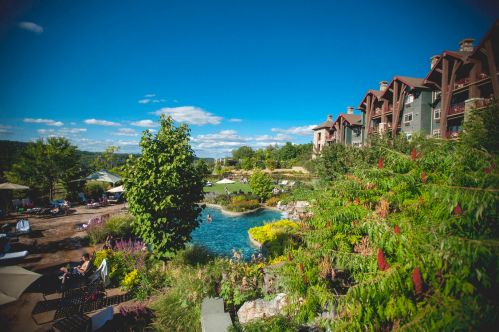 A scenic resort with a pool surrounded by lush greenery and colorful flowers under a clear blue sky.