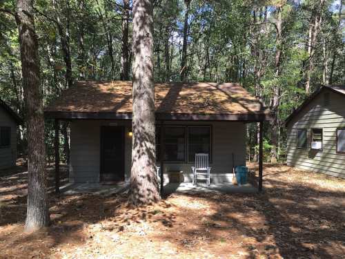 A small cabin surrounded by trees, featuring a porch with a rocking chair and a rustic, natural setting.