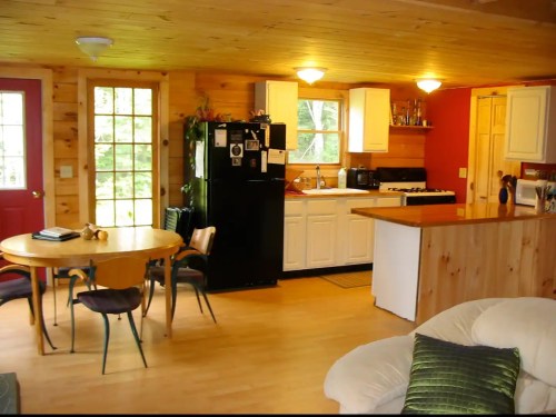 Cozy kitchen and dining area with wooden walls, a round table, and modern appliances in a bright, inviting space.