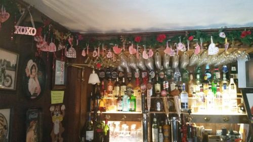 A cozy bar decorated with festive garlands, hanging ornaments, and a variety of bottles on the shelves.