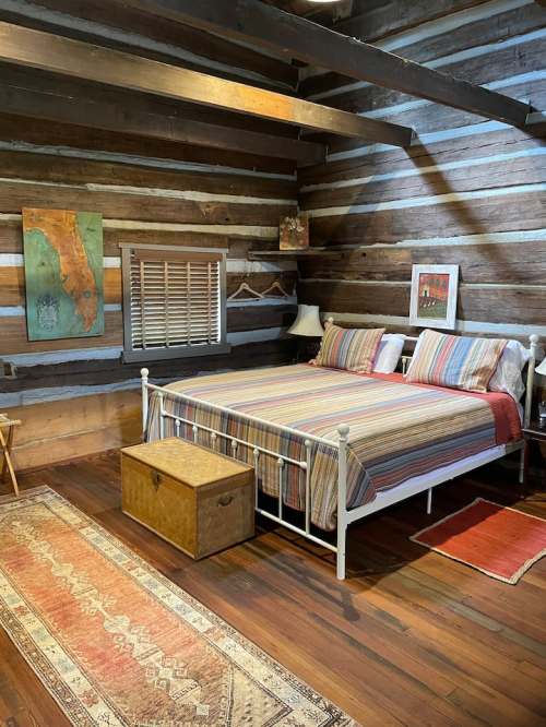 Cozy bedroom with a wooden bed, striped bedding, rustic walls, and a vintage trunk at the foot of the bed.