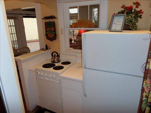 A small kitchen featuring a white refrigerator, stove, and a window with potted plants.