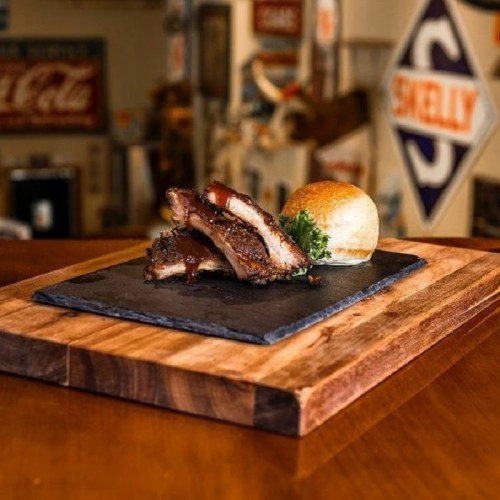 A plate of barbecue ribs with a bun, served on a wooden board against a rustic background.