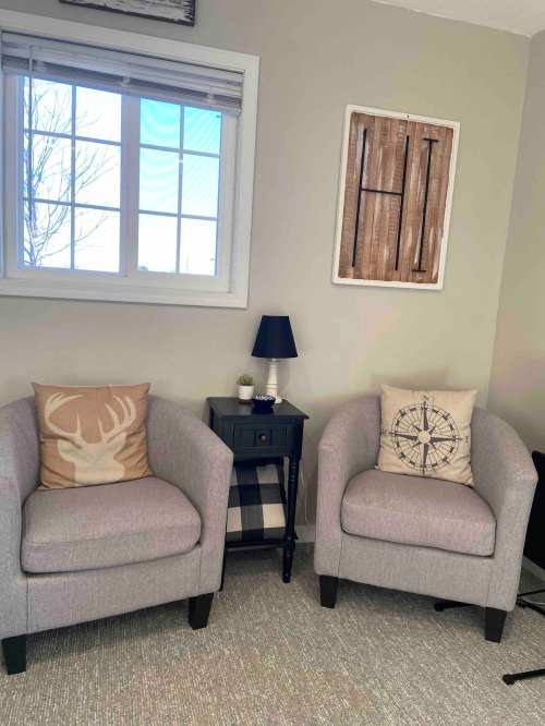 Cozy living space with two gray armchairs, decorative pillows, a small table, and a window letting in natural light.