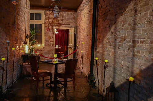 A cozy, dimly lit hallway with brick walls, a table for two, and yellow-lit flower-like candles.