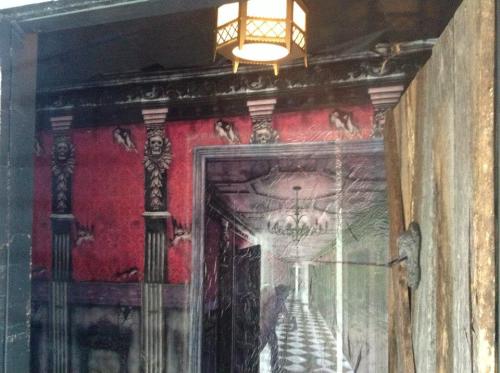 A dimly lit hallway with red wallpaper, ornate columns, and a vintage lamp, creating a mysterious atmosphere.