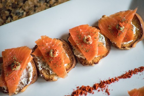 Four slices of toasted bread topped with cream cheese, smoked salmon, and garnished with herbs and spices.