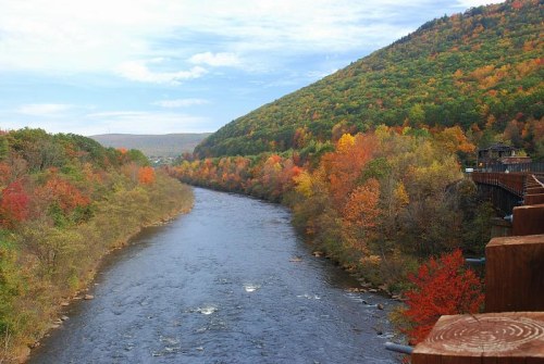 A scenic river flows through a valley surrounded by vibrant autumn foliage on the hillsides.