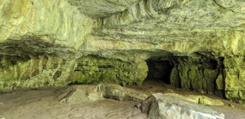 A rocky cave interior with textured walls and a sandy floor, featuring dark openings in the background.