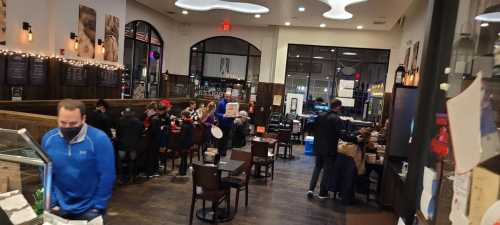 A busy restaurant interior with patrons dining and staff serving, featuring wooden tables and festive decorations.