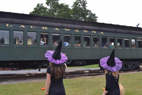 Two children in witch hats watch a vintage train labeled "Lackawanna" as it passes by.