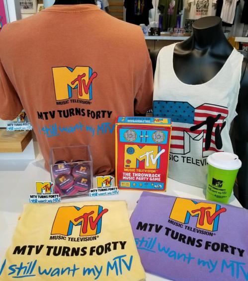 Merchandise display featuring MTV-themed shirts, a party game, and a coffee cup celebrating MTV's 40th anniversary.