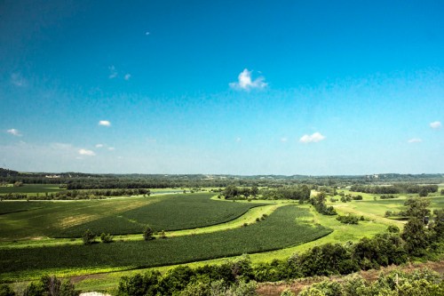 A panoramic view of lush green fields and rolling hills under a clear blue sky with a few scattered clouds.