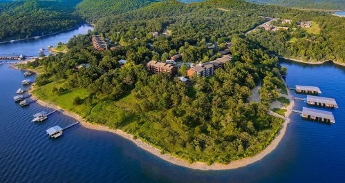 Aerial view of a lush, green island surrounded by water, featuring buildings and boat docks along the shoreline.