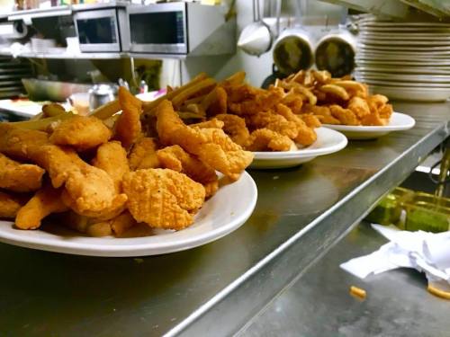 Plates of golden fried chicken tenders stacked on a kitchen counter, ready to be served.
