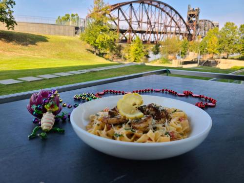 A plate of pasta with shrimp and lemon, set outdoors with a bridge in the background and festive beads nearby.