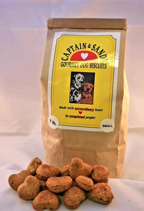 A bag of Captain & Sandy gourmet dog biscuits with heart-shaped treats scattered around it.