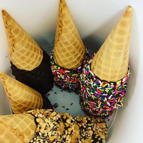 A container holding four ice cream cones: two with chocolate coating, one with colorful sprinkles, and one with nuts.