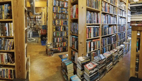 A cozy bookstore with tall wooden shelves filled with books and stacks of books on the floor, creating a warm atmosphere.