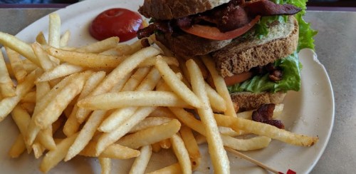 A hearty sandwich with bacon, lettuce, and tomato, served with a side of crispy French fries and a small ketchup portion.