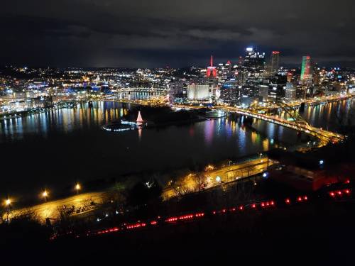 A nighttime view of Pittsburgh's skyline, illuminated buildings, and rivers reflecting city lights.