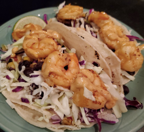 Three shrimp tacos topped with cabbage and a creamy sauce, served with a lime wedge on a blue plate.