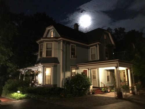 A charming blue Victorian house illuminated by moonlight on a clear night, surrounded by trees.