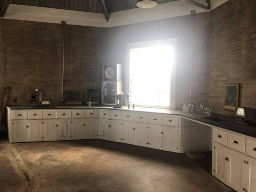 A spacious kitchen with white cabinets, large window, and exposed brick walls, featuring minimal decor and natural light.