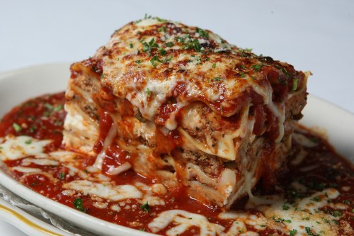 A hearty slice of lasagna topped with melted cheese and marinara sauce, garnished with herbs on a white plate.