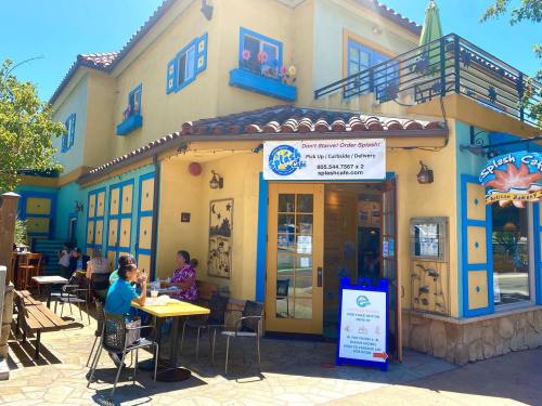 A colorful restaurant exterior with outdoor seating, featuring blue and yellow walls and a sign for takeout orders.