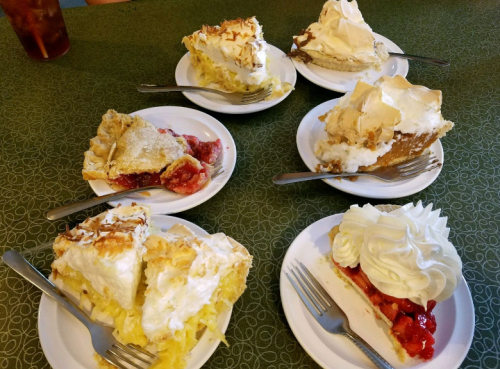 A table with six plates of various pies, including coconut cream and cherry, each topped with whipped cream.