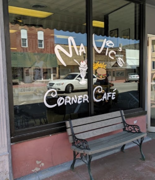 A storefront with "Mavico's Corner Café" sign, featuring a burger and milkshake graphic, and a bench outside.