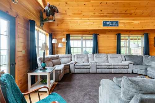 Cozy living room with wooden walls, large sectional sofa, and windows letting in natural light.